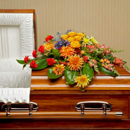 Bright orange and yellow casket spray with red and blue flowers on a wooden casket