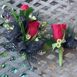 Two red rose boutonnieres with black ribbon accents on a metal table