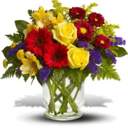 Bouquet of yellow roses, red gerberas, and purple filler in a glass vase