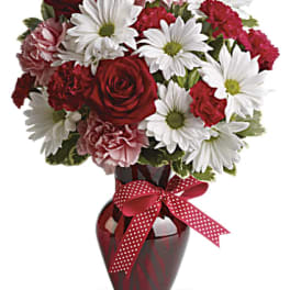 Red and white bouquet in a red glass vase with a polka-dot ribbon