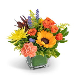 Mixed bouquet in a square glass vase with orange, yellow, and peach flowers