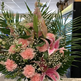 Tall pink floral arrangement in a white container with palm fronds