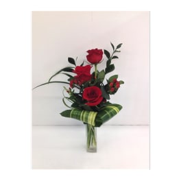 Red roses arranged in a clear glass vase with striped leaf wrapping