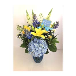 Blue and yellow flower arrangement in a glass vase with a "It's a Boy!" sign