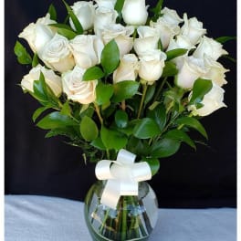 White roses arranged in a glass vase with a white ribbon
