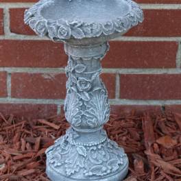 Decorative gray stone pedestal birdbath with floral reliefs