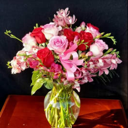 Pink and red roses with orchids in a glass vase