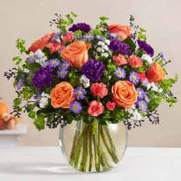 Bouquet of orange roses, purple flowers, and pink carnations in a glass vase