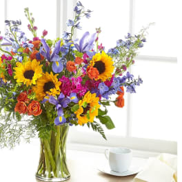 Colorful bouquet of sunflowers, roses, and purple flowers in a glass vase