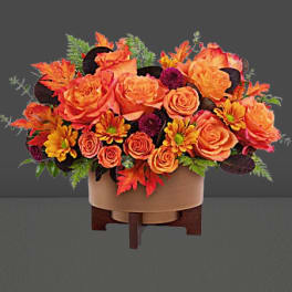 Orange roses and autumn flowers in a round container