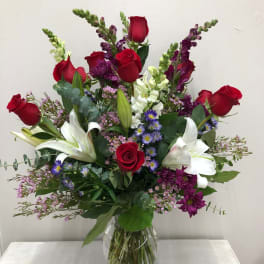 Mixed bouquet of red roses, white lilies, and purple flowers in a glass vase