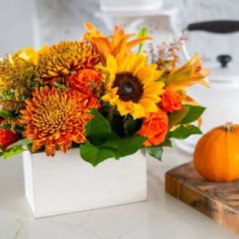 Orange and yellow autumn bouquet in a white box beside a small pumpkin
