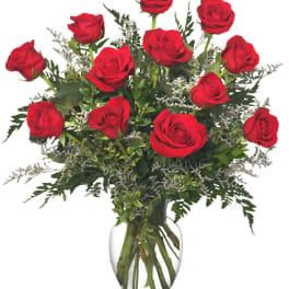 Red roses arranged in a clear glass vase with greenery