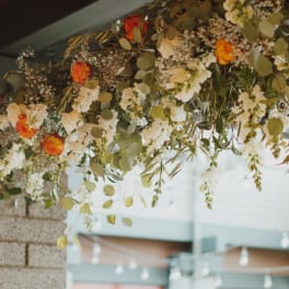 Hanging floral arrangement with orange and white roses and trailing greenery
