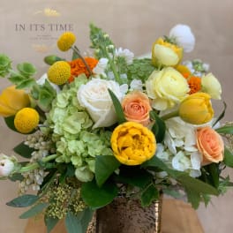 Mixed bouquet in a square ceramic vase with yellow, white, peach, and green blooms