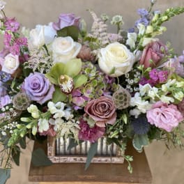 Mixed pastel bouquet with roses, orchids, and snapdragons in a rustic container