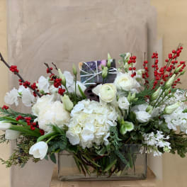 White floral arrangement with red berry branches in a glass vase