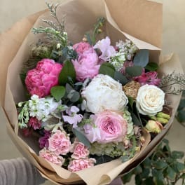 Hand-tied bouquet of pink and white flowers wrapped in brown paper