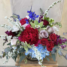 Mixed bouquet of red roses, blue hydrangea, and white filler flowers in a glass vase