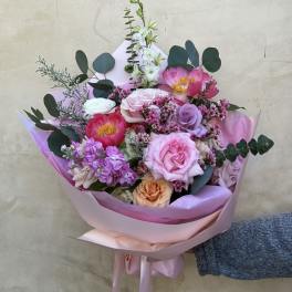 Hand-tied bouquet of pink, lavender, and peach flowers wrapped in pink paper