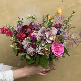 Handheld bouquet of pink, purple, and burgundy flowers