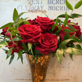 Red roses arranged in a gold vase with green foliage