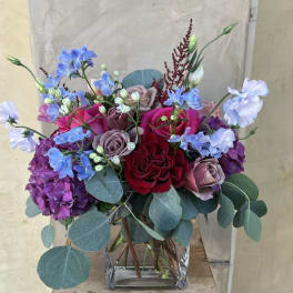 Mixed bouquet of roses, hydrangeas, and blue flowers in a glass vase