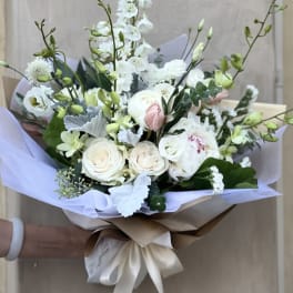 Hand-tied bouquet of white and blush flowers wrapped in lavender paper