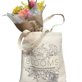 Small bouquet of pink and yellow flowers in brown paper, tucked into a canvas tote bag