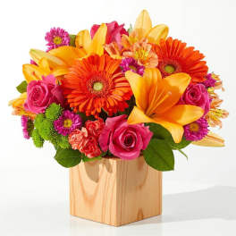 Bright mixed bouquet in a wooden cube vase with roses and lilies
