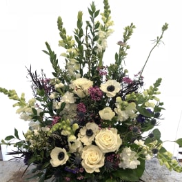 Tall floral arrangement with cream roses, white anemones, and pale snapdragons