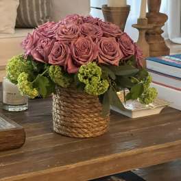 Pink rose arrangement in a woven basket with green blooms