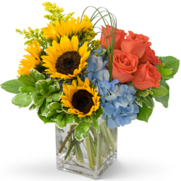 Bouquet of sunflowers, blue hydrangeas, and coral roses in a glass vase