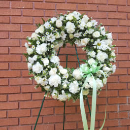 White floral wreath on a stand with a pale green ribbon