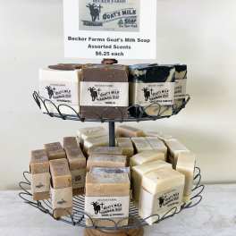 Two-tiered wire stand displaying assorted goat's milk soap bars with beige labels.