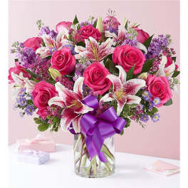 Pink roses and white lilies in a glass vase with a purple ribbon