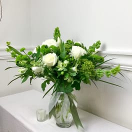 White and green floral arrangement in a glass vase with a ribbon