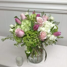 Pink roses and tulips with white hydrangeas in a clear glass vase on a table