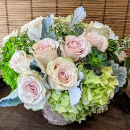 Low arrangement of blush roses, green hydrangeas, and succulents in a rustic container