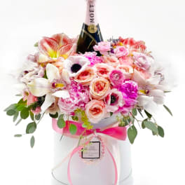 Pink and white flower arrangement in a round box with a Moët bottle