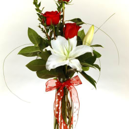 Red roses and a white lily in a clear vase with a red ribbon