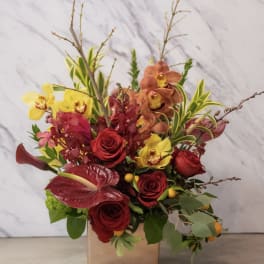 Mixed bouquet of red roses, yellow orchids, and burgundy anthurium in a square vase