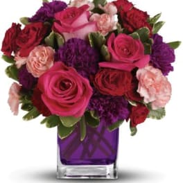 Pink and red roses with purple carnations in a purple glass vase