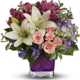Bouquet of white lilies, pink roses, and purple flowers in a purple glass vase
