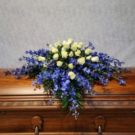 White roses and blue flowers arranged on a wooden casket