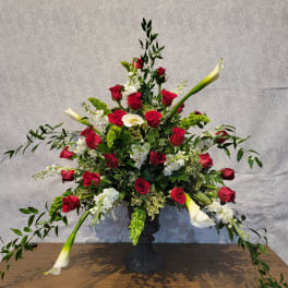 Tall floral arrangement with red roses and white calla lilies in a black urn