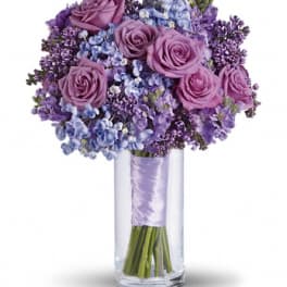 Purple roses and blue flowers in a clear glass vase
