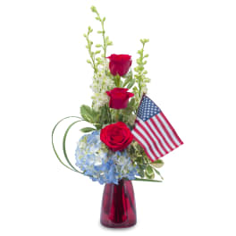 Red roses and blue hydrangeas in a red vase with a small American flag