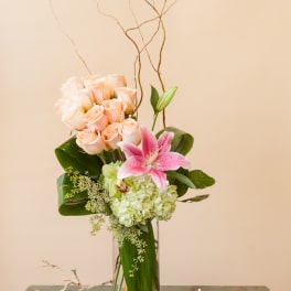 Tall bouquet of peach roses and pink lily in a glass vase
