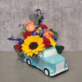 Flower arrangement in a blue truck-shaped container with sunflowers and roses